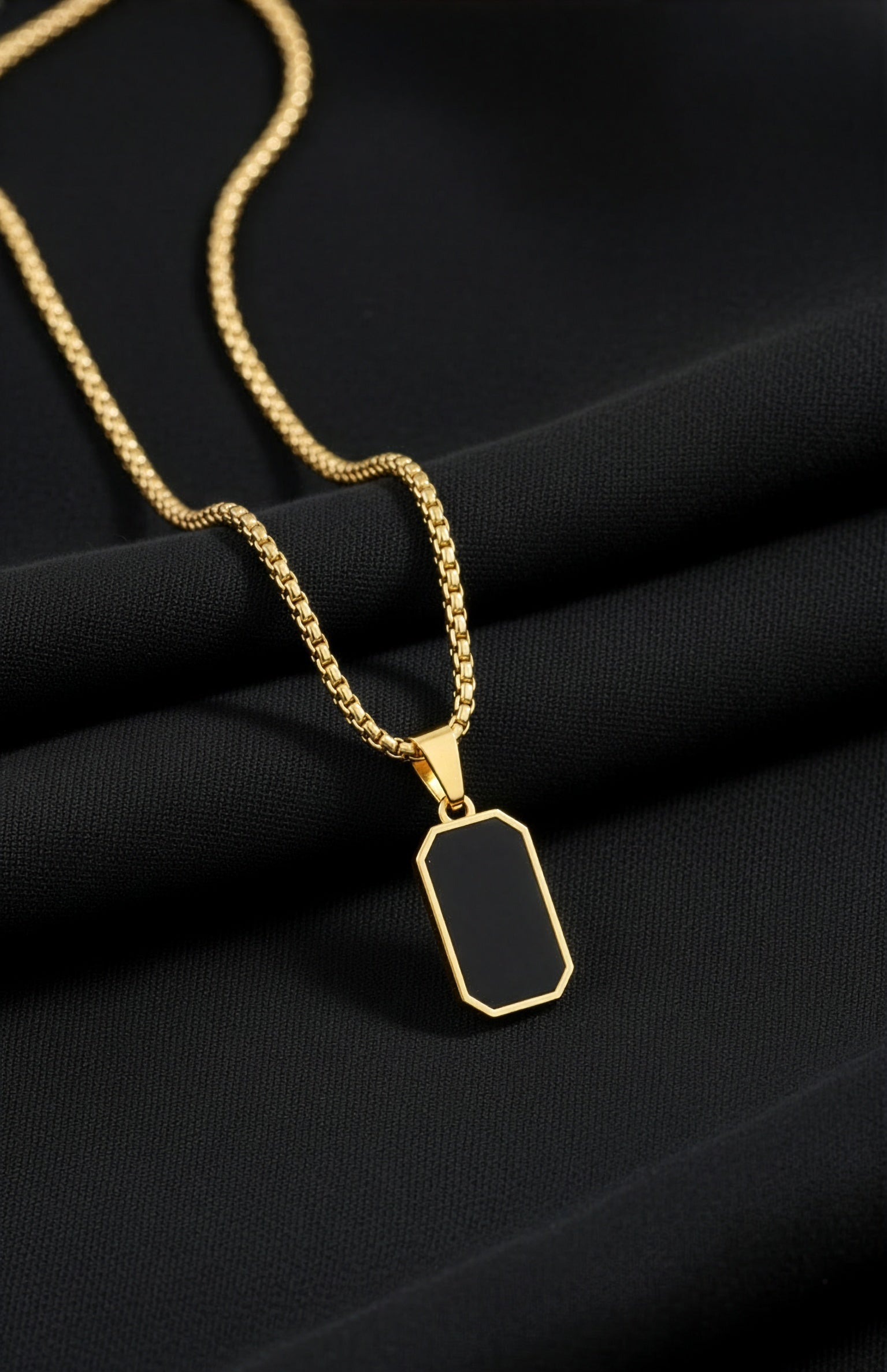 Gold necklace with a black pendant on a black fabric background