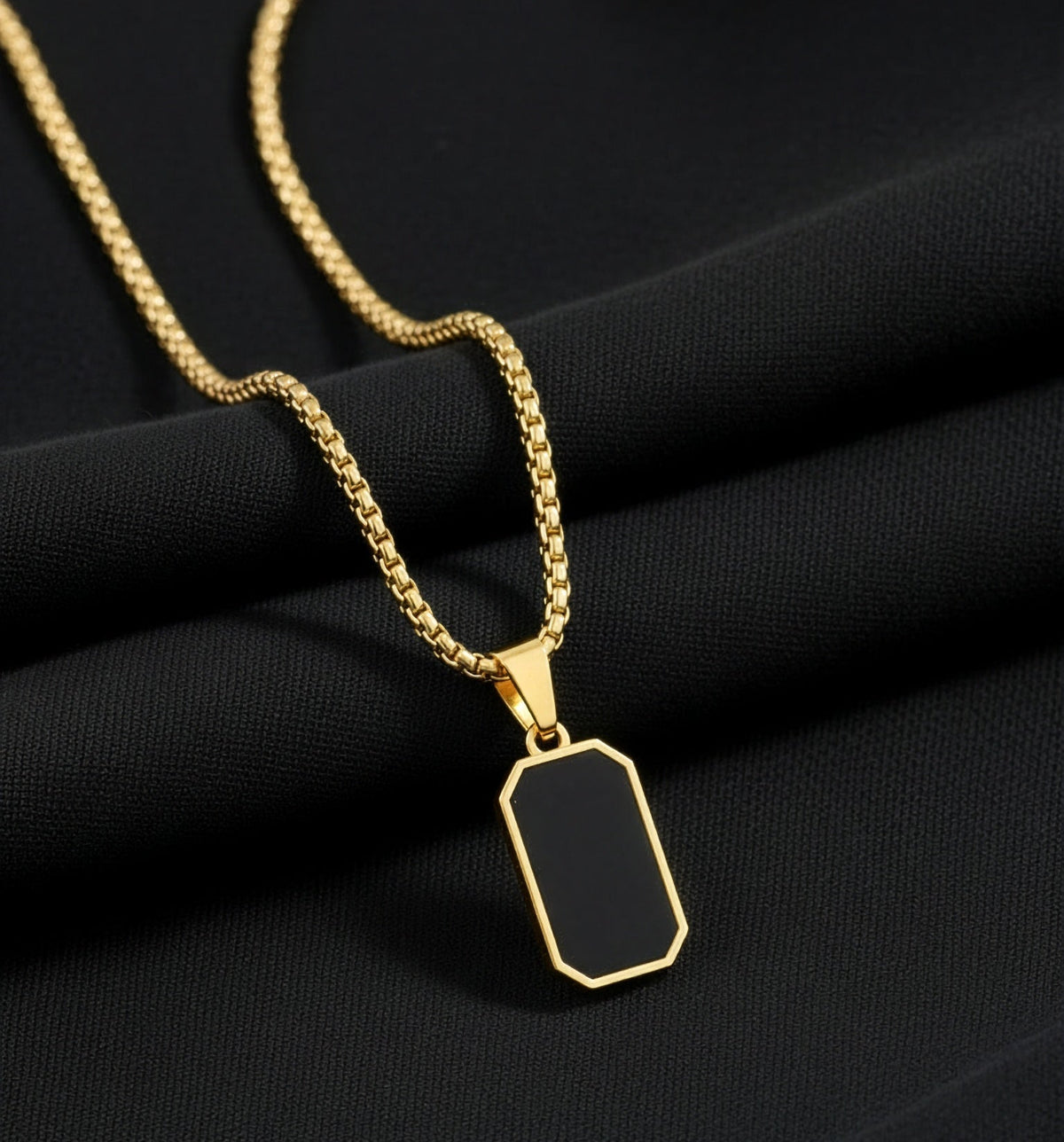 Gold necklace with a black pendant on a black fabric background
