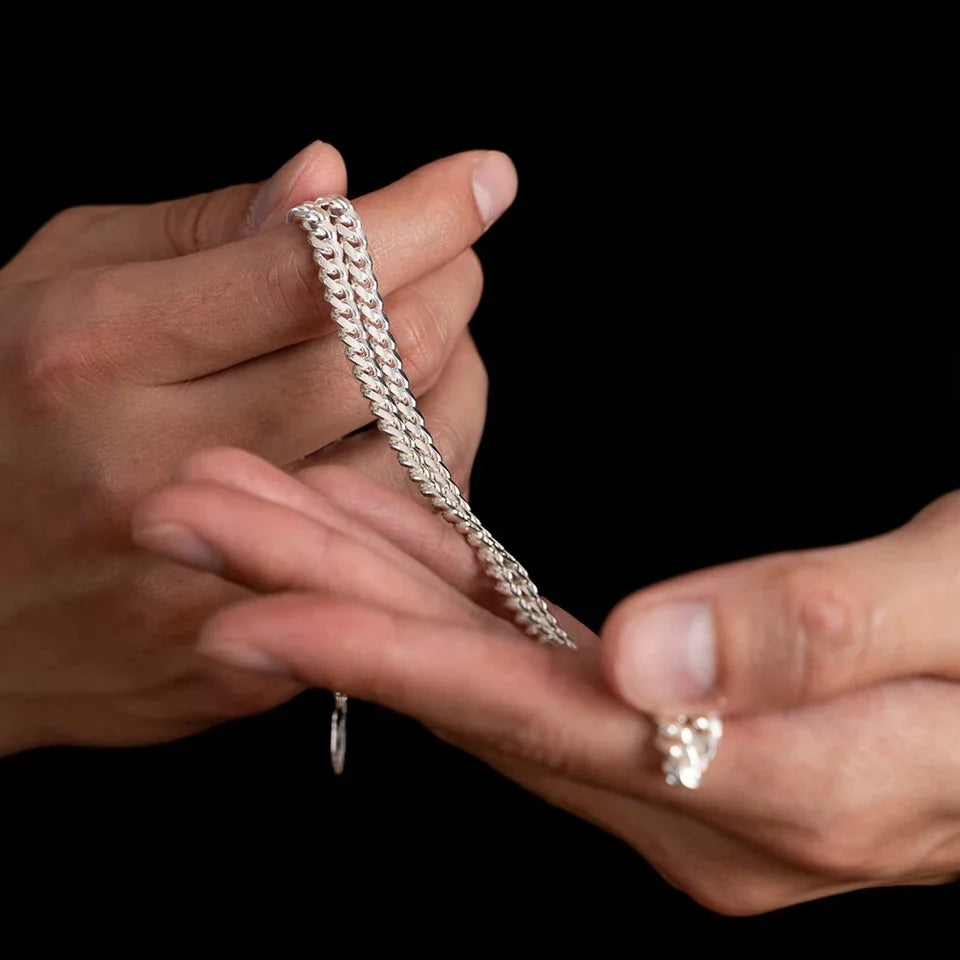 Silver chain necklace held between two hands against a black background