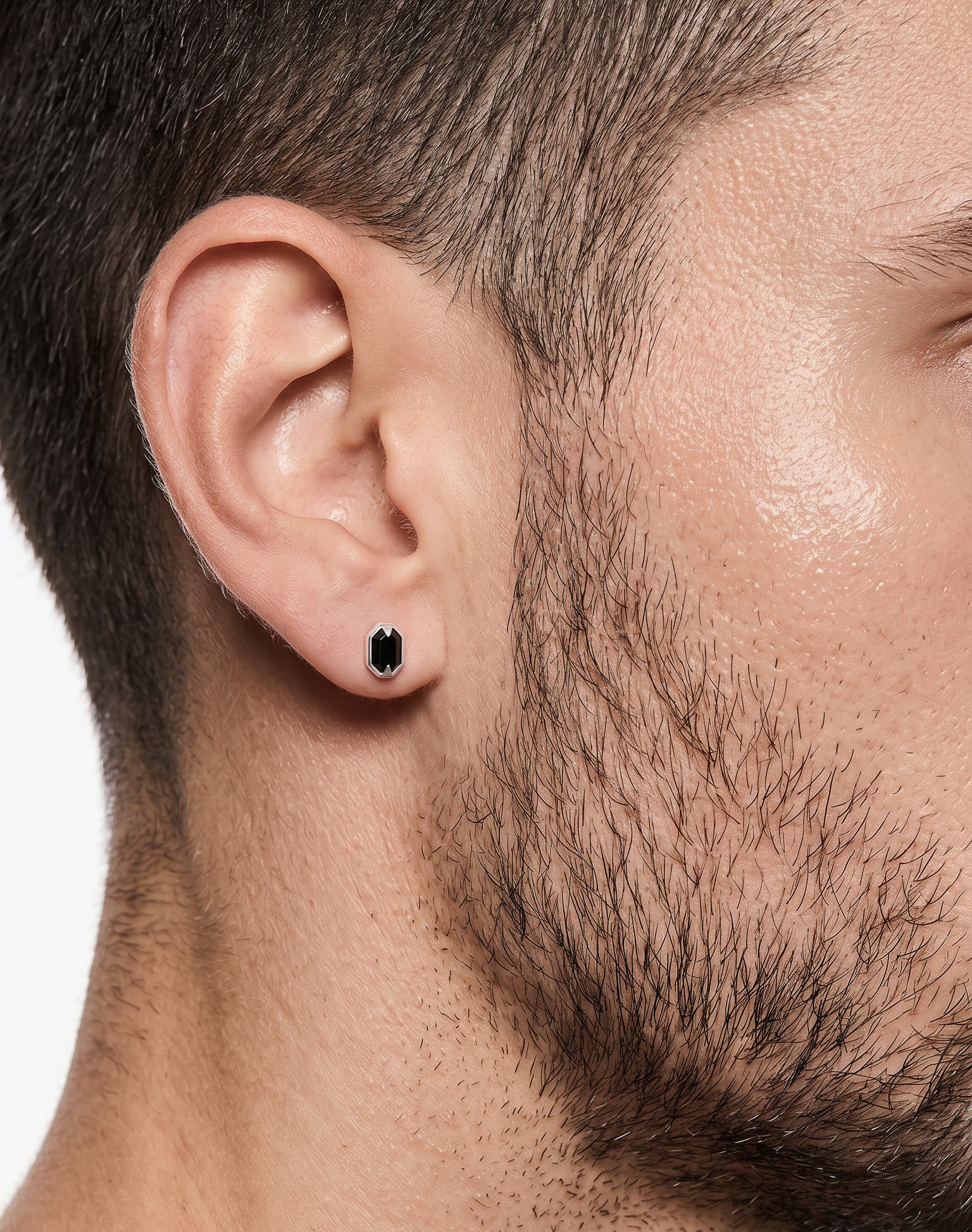 Close-up of a man wearing a black stud earring on a white background