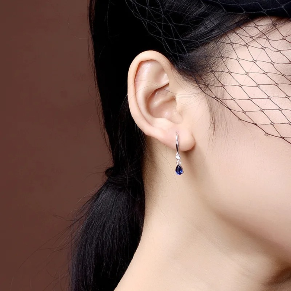 Close-up of an ear wearing a blue gemstone earring with a blurred background