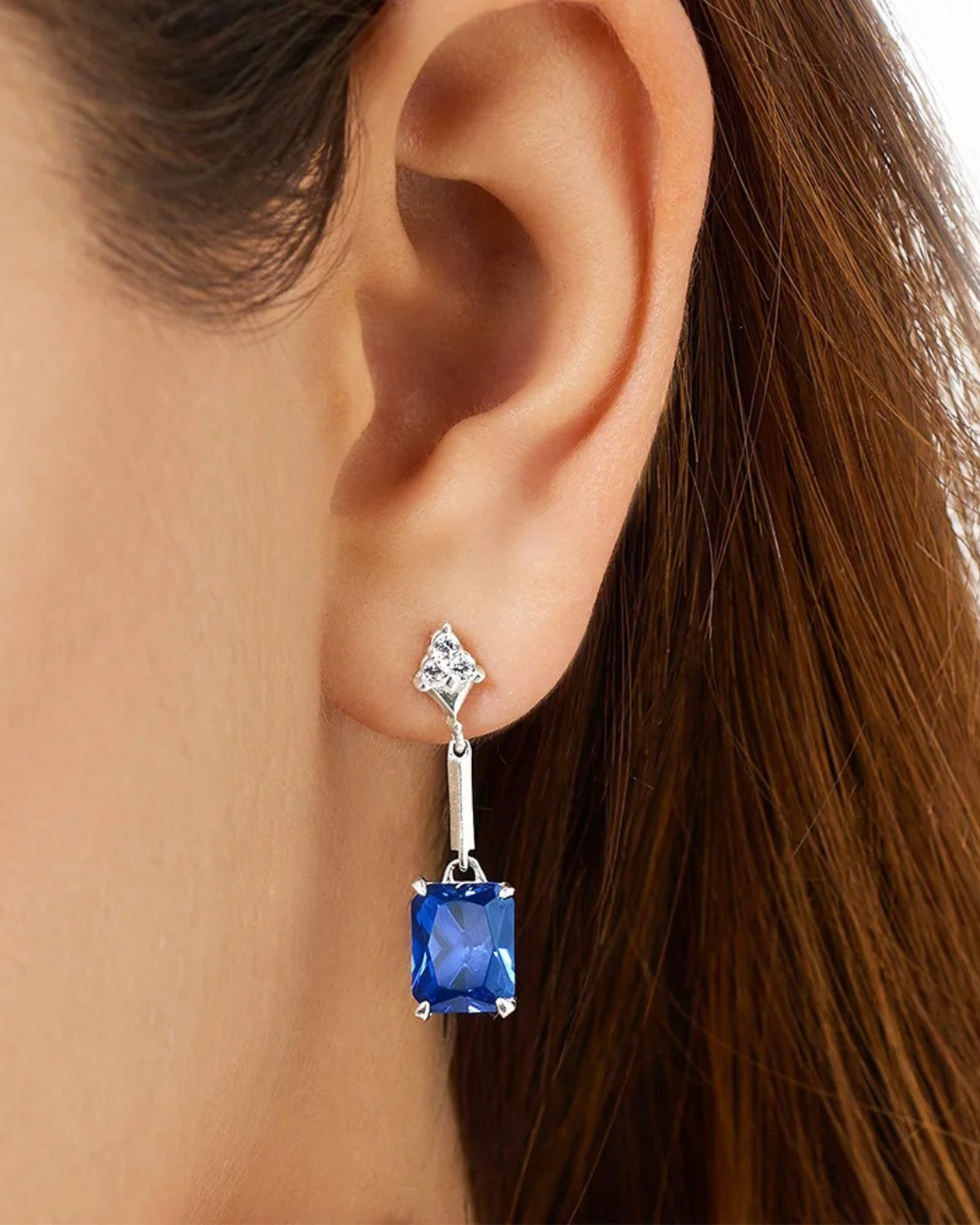 Blue gemstone earring worn by a person with brown hair.