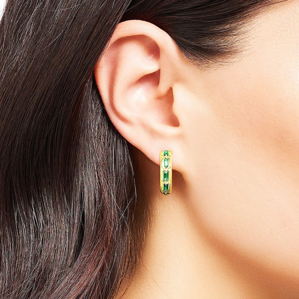 Close-up of an ear wearing a green hoop earring with dark hair.
